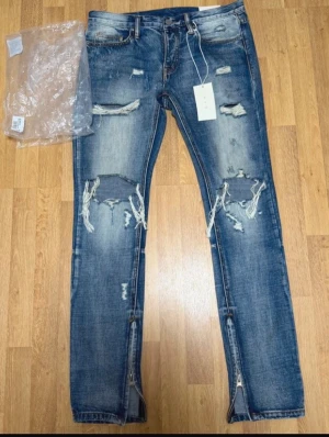 Säljer ett par MNML Ripped Jeans Blue – Size W32 - Jeansen är helt nya och endast testade. Inga skador eller slitage.  Trendiga jeans med ripped design, detaljerade slitningar och dragkedjor vid anklarna – perfekt för en modern streetwear-look. Original tags medföljer.  Size: W32 🏷️ Rabatt vid köp av flera plagg!