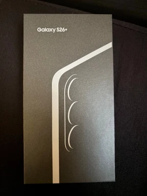 Samsung Galaxy S26+ mobiltelefon 512Gb - Snygg Samsung Galaxy S26+ i svart, levereras i originalförpackning. Lådan har en stilren design med silverdetaljer och visar att mobilen har trippelkamera. Perfekt för dig som vill ha en modern smartphone med grymma funktioner och elegant look. Ny oöppnad 