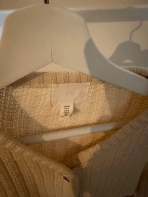 Beige stickad tröja från H&M - En beige stickad tröja från H&M med lång ärm och ribbade muddar. Tröjan har en mjuk struktur och är tillverkad i ett grovt stickat material. Enkel och stilren design som passar perfekt till jeans eller kjol.