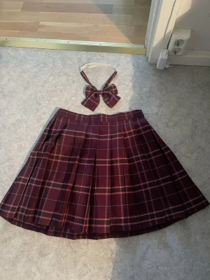 Vinröd rutig plisserad kjol - Säljer en vinröd plisserad kjol med klassiskt rutmönster i rött, vitt och rosa. Kjolen är kort och har en snygg skoluniforms-vibe. Materialet känns som polyester och kjolen har en mörk färgton. Skoluniform stil från Aliexpress för 145kr, använt fåtal gånger utan defekter. Justerbar storlek med en inbyggd ficka. Stl 40 (XL) men går att ändra