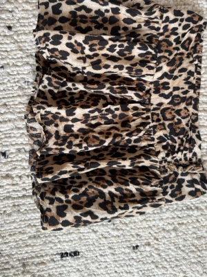 Leopardmönstrad kortkjol med volang - Snygg kortkjol med leopardmönster och volangdetaljer. Kjolen har en smockad midja som ger en bekväm passform och är perfekt för dig som vill sticka ut. Materialet känns mjukt och följsamt mot huden. Den är använd endast en gång på spexdagen i femman🙌🏻🥰🐆 nytt skick💥🫶🏻