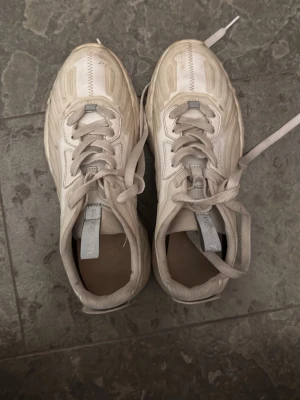 Vita sneakers från Axel  - Säljer ett par vita sneakers från Axel  med chunky sula och snygga detaljer på ovandelen. Skorna har klassisk snörning och är tillverkade i en mix av läder och textil. Perfekta för dig som gillar stilrena och moderna sneakers.