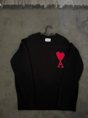 Ami Paris Heart Logo Stickad Tröja Svart  - Helt ny Ami Paris stickad tröja i svart. Aldrig använd och i perfekt skick.  Säljs eftersom den inte kommer till användning och jag behöver rensa garderoben. Klassisk modell med den ikoniska Ami de Coeur-loggan på bröstet.  Skicka gärna meddelande vid frågor eller om du vill ha fler bilder.