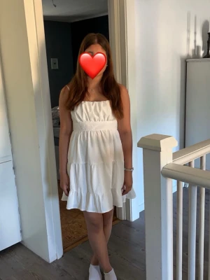 Vit sommarklänning med volang - Söt vit kortklänning med volangkant och smockad överdel. Klänningen är ärmlös och har en luftig passform, perfekt för varma dagar. Enkel och stilren design som passar till många tillfällen. endast använd 2 gånger 
