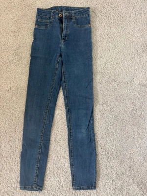 Blå skinny jeans från Gina Tricot - Säljer ett par klassiska blå skinny jeans från Gina Tricot. Jeansen har hög midja, fem fickor och dragkedja med knapp. Tillverkade i stretchigt denim för en bekväm passform.