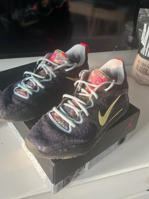 Nike LeBron 7 sneakers svart/guld - Nike LeBron 7 sneakers i svart mesh med guld Swoosh och färgglada detaljer på plösen. Skorna har vita snören och röda detaljer på hälen med '07'-märkning. Snygg och sportig modell med låg profil och unik design.