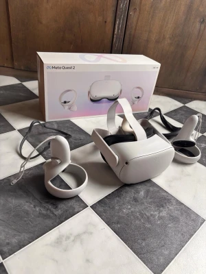 Meta Quest 2 VR-headset med kontroller - Meta Quest 2 VR-headset i vit plast med justerbart huvudband och två matchande handkontroller. Modern design och trådlös frihet för gaming och VR-upplevelser. Levereras med originalkartong och allt som behövs för att komma igång direkt.