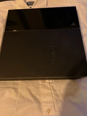 PlayStation 4 svart spelkonsol - Säljer en svart PlayStation 4 från Sony. Konsolen har en stilren, kantig design med en matt och blank finish på ovansidan. Perfekt för gaming och streaming. Tillverkad i plast och passar till alla PS4-spel.