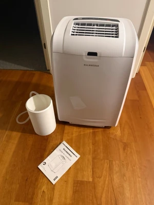 Vit portabel AC från Malmbergs - Säljer en vit portabel luftkonditionering från Malmbergs. AC:n har en modern design med ventilationsgaller upptill och medföljande slang samt instruktionsbok. Perfekt för att kyla ner rummet under varma dagar.