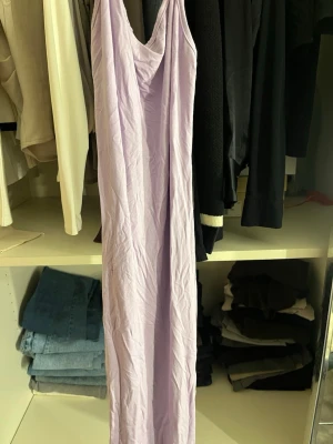Ljuslila långklänning med v-ringning - Säljer en elegant långklänning i ljuslila nyans med v-ringad hals. Klänningen är ärmlös och har en rak, enkel siluett som ger en stilren look. Perfekt för dig som gillar minimalistisk stil och mjuka pastellfärger.