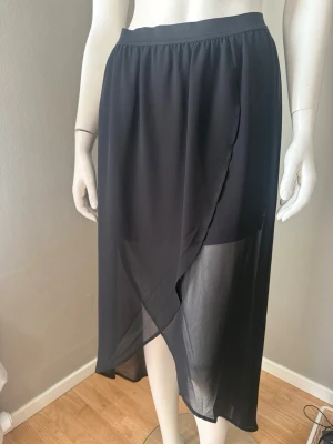 Svart i transparent tyg strl 38  - Snygg svart midikjol  med transparent, lätt material. Kjolen har resår i midjan och ett elegant fall som ger en luftig känsla. Perfekt för dig som gillar stilrena och trendiga plagg.