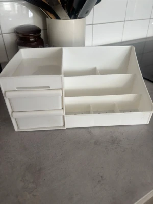 Vit sminkorganiserare med lådor - Praktisk sminkorganiserare i vit plast med flera fack och 2 utdragbara lådor. Perfekt för att hålla ordning på borstar, smink och små tillbehör. Modern och stilren design som passar på sminkbordet eller i badrummet.