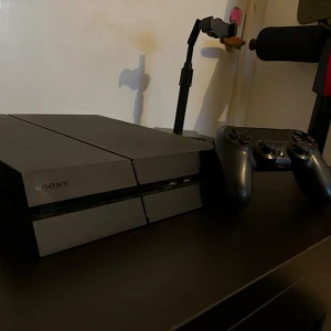 PlayStation 4 med svart handkontroll - Säljer en PlayStation 4 i mattsvart färg med tillhörande svart DualShock 4-handkontroll. Konsolen har den klassiska kantiga designen och är tillverkad i plast. Perfekt för gaming och streaming hemma.