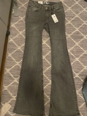 Gråa bootcut jeans med utsvängda ben - Snygga gråa jeans med bootcut-modell och utsvängda ben. Klassisk femficksdesign, hällor för bälte och knappgylf. Perfekta för dig som gillar en retroinspirerad look och vill sticka ut lite extra.