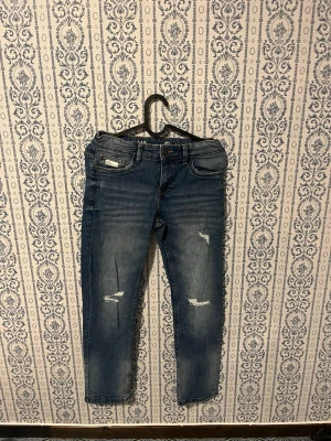 Blå slitna jeans från LAB Industries - Säljer ett par blå jeans från LAB Industries i regular fit. Jeansen har slitna detaljer på benen och klassisk femficksdesign. Perfekta för en avslappnad och trendig look. Materialet är denim med snygg tvätt och lagom stretch.