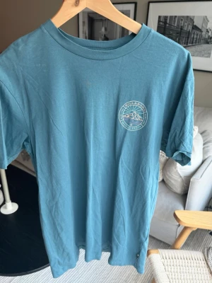 Blå t-shirt från Billabong - Säljer en blå t-shirt från Billabong med rund hals och tryckt logga på bröstet. T-shirten har en avslappnad passform och är tillverkad i mjuk bomull, perfekt för en chill och stilren look.