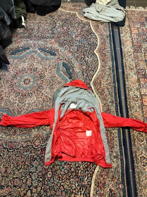 Moncler Röd vindjacka  - Snygg röd vindjacka med grå insida och huva. Jackan har dragkedja, justerbart midjeband med röd, vit och blå detalj samt praktiska fickor. Materialet är tunt och lätt, perfekt för blåsiga dagar. Passar dig som vill ha en sportig och stilren look.