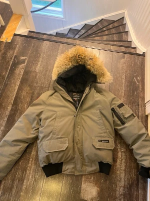 Canada Goose grön dunjacka med päls - Säljer en grön dunjacka från Canada Goose med stor huva och äkta päls. Jackan har flera fickor, ribbade muddar och klassisk Canada Goose-logga på ärmen. Perfekt för kalla vinterdagar och riktigt varm. Storlek S. Skriv om ni har några frågor! Pris kan diskuteras.