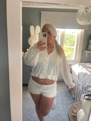 Vit blus med volang och resår - Säljer en söt vit blus med lång ärm, volangdetalj nedtill och resår i midjan. Blusen har en avslappnad passform och lätt struktur i tyget. Perfekt till sommaren och enkel att styla med shorts eller jeans.