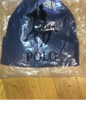 Mörkblå mössa från Polo Ralph Lauren - Snygg mörkblå ribbstickad mössa från Polo Ralph Lauren med klassisk logga framtill. Mössan har uppvikt kant och är tillverkad i mjukt material som håller dig varm. Perfekt accessoar för kyliga dagar och enkel att matcha med olika outfits.