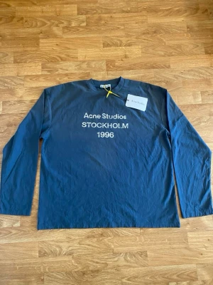 Blå tröja Acne Studios  - Mörkblå långärmad tröja från Acne Studios med vit text 'Acne Studios STOCKHOLM 1996' på bröstet. priset kan diskuteras 