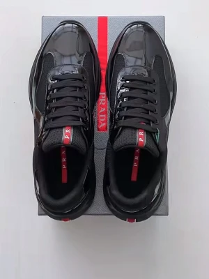 Svarta sneakers från Prada - Snygga svarta sneakers från Prada med glansig finish och meshdetaljer. Skorna har svarta snören och en röd logotypremsa på plösen. Modern och sportig design som sticker ut med exklusiv känsla.