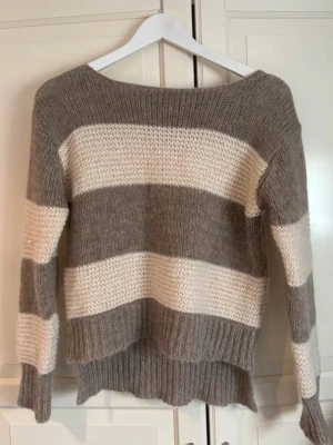Stickad tröja med breda ränder STOCKH LM - Stickad tröja från STOCKH LM i storlek S. Tröjan har breda horisontella ränder i beige och offwhite, rund halsringning och ribbstickad nederkant. Mjuk och skön kvalitet, perfekt för kyliga dagar.