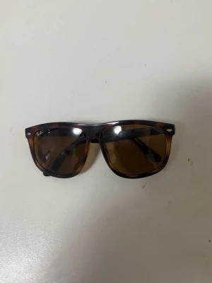 Bruna Wayfarer solglasögon Ray-Ban - Snygga Wayfarer solglasögon från Ray-Ban med brunmelerad båge och mörka glas. Klassisk och tidlös design som passar till det mesta. Ray-Ban-logga syns på både glaset och skalmen. Perfekta för soliga dagar!