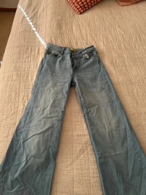Ljusblåa utsvängda jeans - Säljer ett par ljusblå jeans med utsvängda ben och klassisk femficksmodell. Jeansen har mellan hög midja och dragkedja med knapp framtill 👖🩵