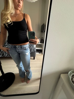 Ljusblå slitna bootcut jeans, Gina -  Är i storlek 164 men skulle säga passar XS-S. Säljer ett par ljusblå bootcut jeans med slitningar och hål vid knäna. Jeansen har röda kontrastsömmar och klassisk femficksdesign. Perfekta för en avslappnad och trendig look. Materialet är denim i bomull.