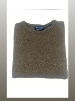 Olivgrön stickad tröja Marc O'Polo - Olivgrön stickad tröja från Marc O'Polo med rund halsringning och diskret broderad logga på bröstet. Tröjan har en klassisk passform och är tillverkad i mjukt material som passar perfekt till kyligare dagar.långarmad