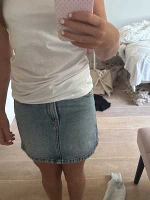 Blå jeanskjol med fickor - Säljer en klassisk blå jeanskjol  i kort modell med två bakfickor och en enkel söm framtill. Kjolen är gjord i denim och är ganska kort, perfekt till sommaren. Den är midweist och är från Tom Tailor. Den är använd ett fåtal gånger innan den blev för liten. Nypris 450 kronor på Zalando!