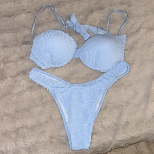 Oanvänd Ljusblå bikini med textur och knyt - Superfin ljusblå bikini med vadderad topp och högt skurna trosor. Bikinin har en snygg ribbad textur och knyt i nacken. Perfekt för stranden eller poolen, och den ljusa blå färgen ger en fräsch vibe. Materialet känns mjukt och stretchigt för bästa komfort oanvänd. Mindre i storlek