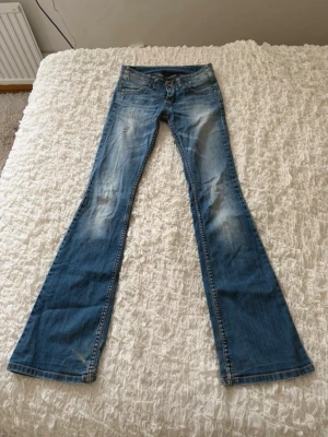 Supercoola lågmidjade bootcut jeans  - Säljer ett par sjukt coola lågmidjade bootcut jeans. De har en snygg ljus wash framtill samt nitar och tryck vid fickorna. Coola detaljer med nitar på bakfickorna och ett coolt tryck på linningen där bak. Sitter riktigt snyggt. De är i jättefint skick. Midjemåttet är 35cm och innerbenslängden är 84cm. Materialet har lite flex i sig så midjemåttet kan flexa lite. Skriv bara om du har några frågor, jag fraktar snabbt!💕💕