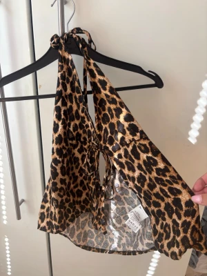 Leopardmönstrad halterneck topp - Snygg leopardmönstrad halterneck topp med knyt i nacken och framtill. Toppen är ärmlös och har en croppad passform, perfekt för dig som vill sticka ut. Materialet känns lätt och svalt, vilket gör den skön att bära under varma dagar.