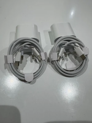 2 st USB-C laddare med kabel - Två stycken vita USB-C laddare med tillhörande flätade USB-C till USB-C kablar. Laddarna har en kompakt och stilren design i plast och kablarna är gråvita med tåligt material. Perfekt för att ladda mobiltelefoner och andra enheter med USB-C.