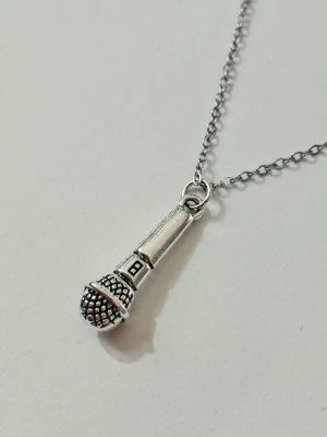 Halsband med mikrofonhänge i silverfärg - Unikt halsband med ett detaljerat mikrofonhänge i silverfärgad metall. Kedjan är supertunn men slitstark och smidig, och hänget har en cool, retroinspirerad design som passar dig som älskar musik och vill sticka ut med din stil. Materialet är rostfritt stål 