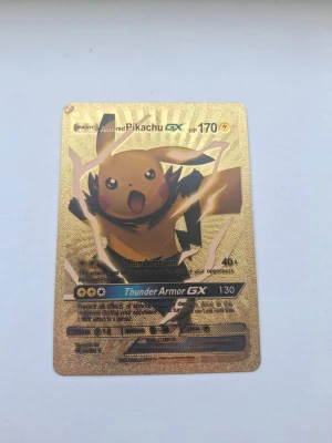 Guldfärgat Pikachu GX Pokémonkort - Unikt guldfärgat Pokémonkort med Pikachu GX och Armored-design. Kortet har detaljer i svart och guld, med text och effekter som Thunder Armor GX och Thunderstorm. Tillverkat i metall med glansig finish, perfekt för samlare eller som coolt tillbehör till spel och konsoler.