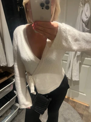Vit omlottkofta med knytband - Säljer en supermjuk vit omlottkofta med knytband i midjan. Koftan har djup v-ringning, långa ärmar och en avslappnad passform. Perfekt att styla med jeans eller kjol för en trendig look.