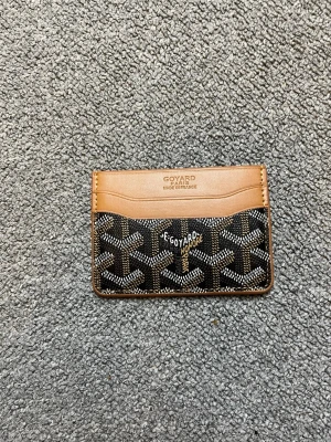 Goyard brun och svart kortfodral - Snyggt kortfodral från Goyard i brunt och svart med klassiskt mönster och detaljer i beige läder. Fodralet har flera kortfack både fram och bak, perfekt för att hålla koll på dina viktigaste kort. Ikonisk logga framtill och stilren design.