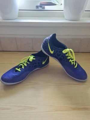 Nike Elastico Pro II Pure Purple/Volt strl 40 - Nike Elastico Pro II är en inomhussko speciellt avsedd för spel på små ytor.  Skon är tillverkad med en skräddarsydd passform efter fotens konturer. Kombinerat med mjukt och flexibelt kalvläder erbjuder denna sko väldigt mycket komfort.  Med en låg och flexibel framfot så får du de allra bästa förutsättningar för att dominera det tekniska spelet inomhus.  Undersulan är designad för att ge extra grepp på golvet vilket ger stor fördel på inomhusplaner. På insidan av skon sitter ett mönster som ger