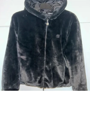 Fila teddy jacka  - (Är finare glansig svart än på bild) Mjuk och fluffig svart pälsjacka från Fila med stor logga på ryggen och dragkedja framtill. Jackan har huva, sidofickor och en clean look som passar perfekt till streetwear. Snygg och varm för kyliga dagar. Finns ej längre att köpa. Nypris 899;-  