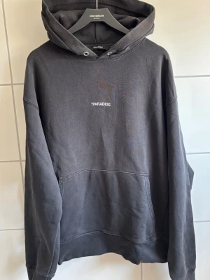 Svart Zadig Voltaire hoodie - Säljer en svart hoodie i storlek M med luva. På bröstet står det 'PARADISE' och på ryggen finns ett stort tryck med texten 'MADONNA INN' i rött och vitt. Hoodien har en avslappnad passform och är gjord i mjukt bomullsmaterial. Bara höra av er vid frågor eller om fler bilder behövs!