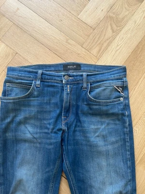 Replay jeans - Snygga blå slim fit jeans från Replay med klassisk femficksdesign och diskreta slitningar framtill. Jeansen har normal midja, dragkedjegylf och är tillverkade i ett stretchigt denimtyg för extra komfort. Perfekta för en avslappnad och trendig look. Märket där bak är borta men byxorna är i ett bra skick 