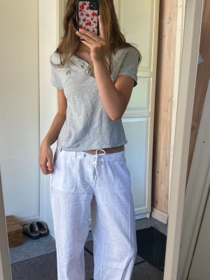 Grå polotopp med kort ärm - Säljer en stilren grå polotopp med korta ärmar och krage. Toppen har knappar framtill och en liten broderad logga på bröstet. Perfekt till jeans eller linnebyxor för en avslappnad look.