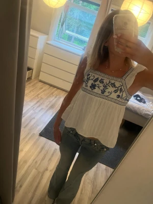 Vit och blå broderad linnetopp SHEIN - Säljer en söt vit linnetopp från SHEIN i storlek XS. Toppen har breda axelband och ett blått broderat mönster över bysten. Luftig och flowy passform, perfekt för varma dagar. Materialet känns lätt och bekvämt mot huden.