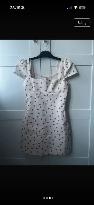 Vit kort prickig klänning med snörning - Helt ny med lappen kvar!💕💕Supersöt kort klänning i vit med bruna prickar och puffärmar. Klänningen har fyrkantig urringning, snörning i ryggen och är figurnära. Perfekt för sommarens alla tillfällen!