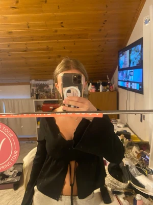 Svart croppad omlottopp - Trendig svart croppad omlottopp med långa ärmar och knyt framtill. Perfekt för dig som vill ha en edgy och stilren look. Toppen har en djup v-ringning och är tillverkad i ett mjukt material som sitter snyggt på kroppen.