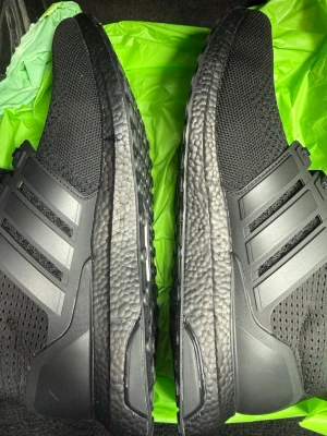 Svarta Adidas Ultraboost sneakers - Säljer ett par helsvarta Adidas Ultraboost sneakers med stickad ovandel och klassiska tre ränder på sidan. Skorna har en tjock, strukturerad sula för extra komfort och en sportig look. Perfekta för dig som gillar stilrena och bekväma sneakers. Kommer utan box.(Pris kan diskuteras) 