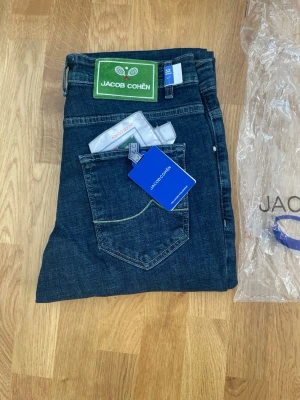 Jacob Cohën mörkblå jeans - Snygga mörkblå jeans från Jacob Cohën med klassisk femficksdesign och kontrastsömmar. Jeansen har knäppning med silverfärgade knappar och detaljerad insida med mönstrad textil. Tillverkade i Italien och har en modern passform.